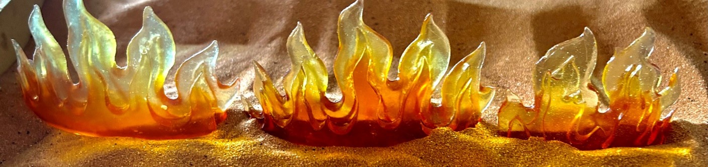 Three red/orange colored miniature fire figurines sitting on a bed of sand