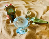 Three figurines sit in sand, a frosted glass globe, a grandfather clock, and a genie's lamp