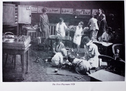 Old black and white image of children and supervisory adults in a classroom-like setting